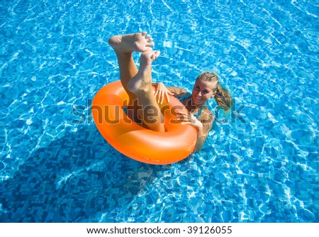 Beautiful blonde girl swimming in hotel pool on inflatable raft