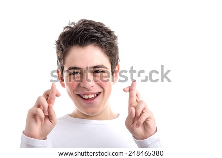 Latin young boy with acne in a white long sleeve t-shirt smiles crossing fingers of both hands as superstitious  gesture to get luck