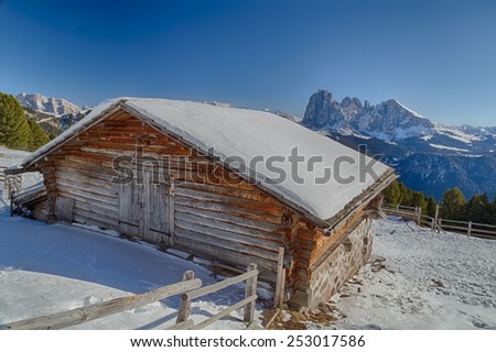 Alpine chalet surrounded by a fence in the snow in front of a panorama of snowy peaks on a bright sunny day in winter