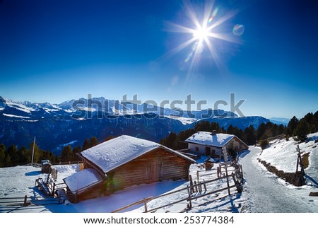 Alpine chalet surrounded by a fence in the snow in front of a panorama of snowy peaks on a bright sunny day in winter on Dolomites Alps