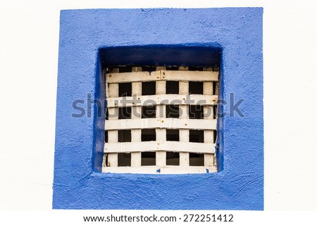 Square window with bright blue painted border and wood grate on white wall