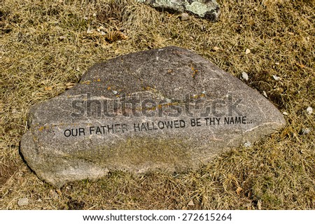 English sentence from The Lord\'s Prayer printed in block letters on a rock on winter grass