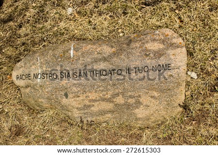 Italian sentence from The Lord\'s Prayer printed in block letters on a rock on winter grass