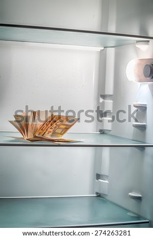 Fresh money in the refrigerator: a handful of 50 euros banknotes illuminated by cold light of an empty refrigerator