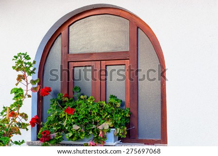Rounded wood frame  window with red geraniums flower pots and white wall