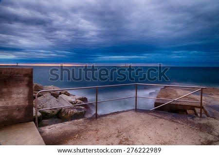 Sunset on breakwater with stairs on the Mediterranean sea with red steel lookout and green top white lighthouse in the cloudy background near Porec in Croatia