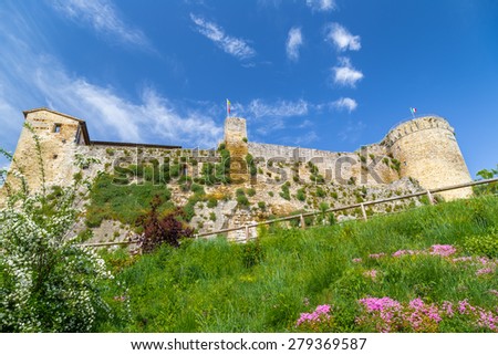 Flowers and plants surrounding a XI century brick walls fortress guarding a small village in the Italian countryside