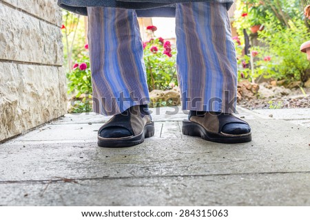 feet of man in brown slippers with blue socks, blue striped pajamas and gray dressing gown in your back yard