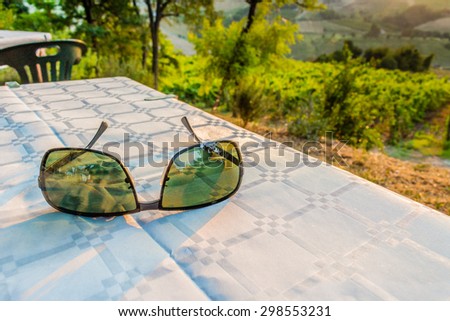 see the world through the eyes of ecology - sunglasses with green lenses on a dinner table with vineyards,farmlands and vegetation in the countryside in the background