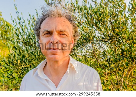 Elegant senior man wearing white shirt among the leaves of olive trees
