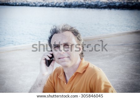 Classy  40 years old sportsman with three-day beard and salt and pepper hair wearing an orange polo shirt while he is sitting on a bench on the pier and holding his head: is it headache?