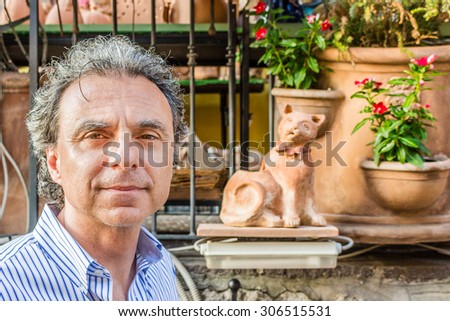 middle-aged man in a striped shirt in front of pots of flowers in Italian village market