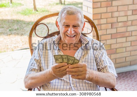 octogenarian elder in checkered shirt is happy while playing cards on the patio of his house in the Italian countryside