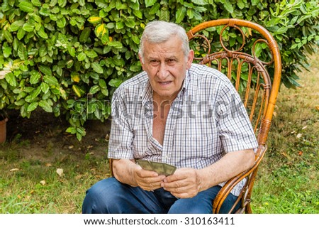 octogenarian elder in checkered shirt is happy while playing cards in the garden of his house in the Italian countryside