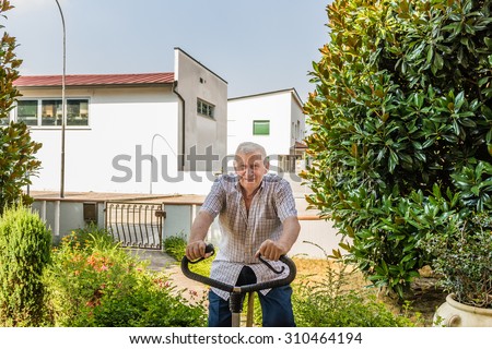 elderly octogenarian male keeps fit by doing exercise bike on the garden of the house