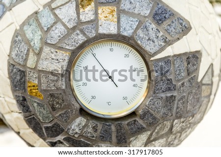 Temperature just below zero Celsius marked by a analogue environmental  thermometer cemented into a mosaic of stones