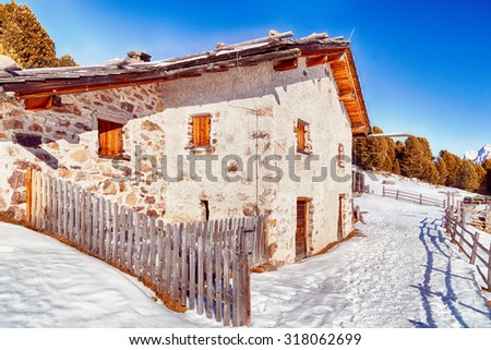 Alpine chalet surrounded by a fence in the snow among snowy peaks and pine forest on a bright sunny day in winter