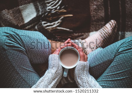 Cozy woman in knitted winter warm socks and in pajamas holding a cup of hot cocoa during resting on checkered plaid blanket at home in winter time. Cozy time and winter drinks. Top view  商業照片 © 