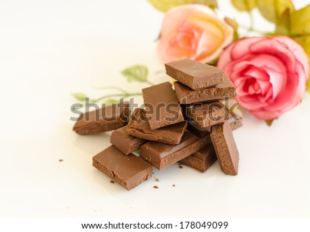 Broken dark chocolate bar and roses isolated on white background.