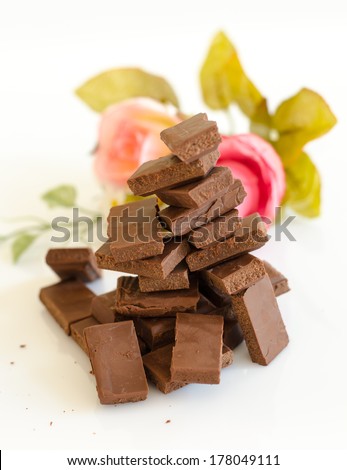 Broken dark chocolate bar and roses isolated on white background.
