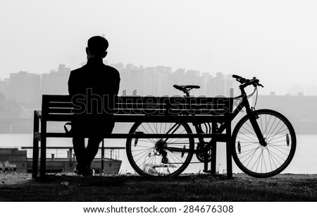 Silhouette in black and white of a man sitting on the bench with his bicycle by the Han river, Korea.