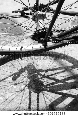 Old bicycle wheel casting a shadow on the ground, black and white.