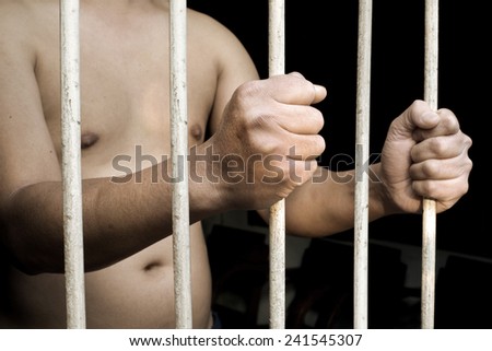 Hands of man prisoner gripping in and out on rusty prison bars