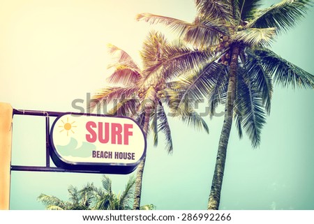 Vintage surf beach house signage and coconut palm tree on tropical beach blue sky with sunlight of morning in summer,  instagram retro filter
