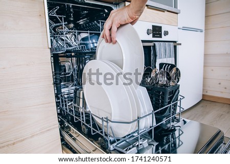 Woman loading the dishwasher. Open dishwasher with clean glasses and dishes close-up after washing. Clean  in open dishwashing machine.