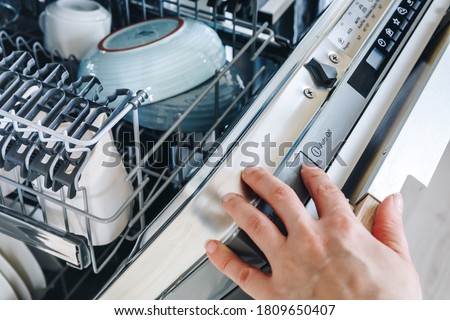 Run the dishwasher machine. Close-up of woman's finger pressing start button on dishwasher in the kitchen.