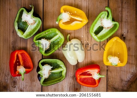 halves of red, green, black, white and yellow bell peppers on wooden background