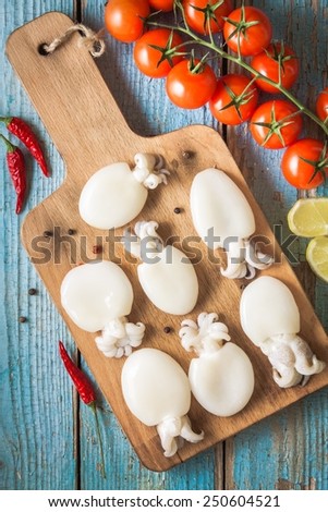 Raw babies cuttlefish  on a cutting board with tomatoes, chili peppers and lemon on  blue rustic background