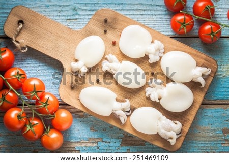 Raw babies cuttlefish  on a cutting board with tomatoes on  blue rustic background