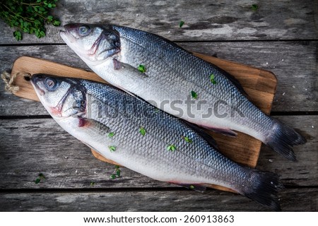 two raw sea bass on a cutting board with fresh thyme on wooden rustic table