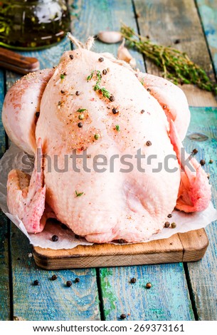 organic raw whole chicken with thyme, pepprs, olive oil on a rustic table