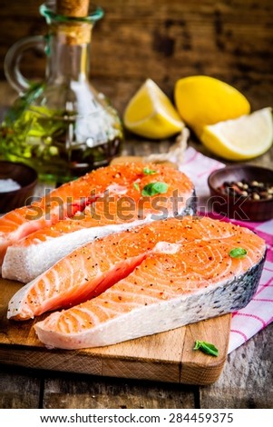 Two fresh raw salmon steaks with lemons and olive oil on wooden cutting board