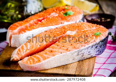 Two fresh raw salmon steaks with peppers on wooden cutting board