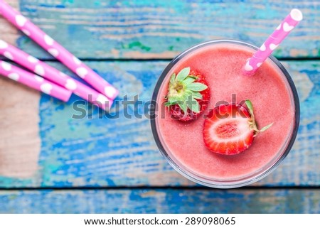 strawberry smoothie in a glass with a straw on a wooden table top view