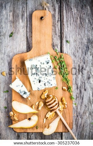 Blue cheese with slices of pear, nuts and honey on wooden cutting board