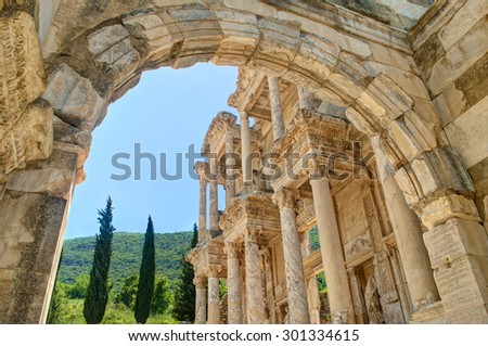view of celsus library facade and green hill with cypress trees and blue sky through arch in Ephesus, Turkey