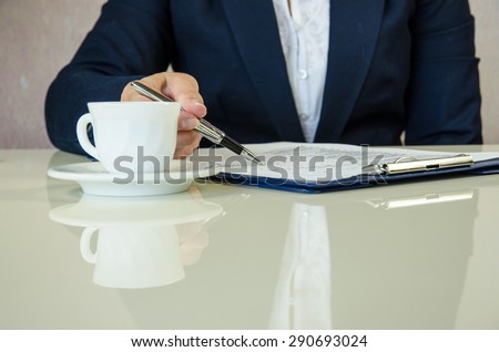 hand with pen writing on paper and mug with coffee
