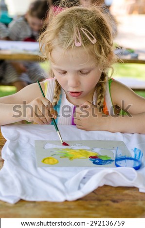 beautiful blond girl painting with brush into t-shirt with colorful colors