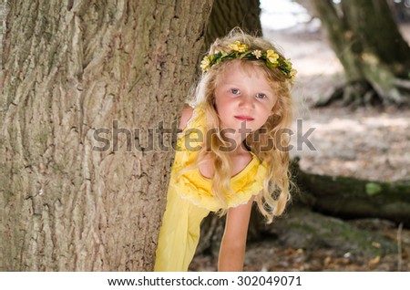 beautiful girl with long hair and flower headband leaned to the tree trunk