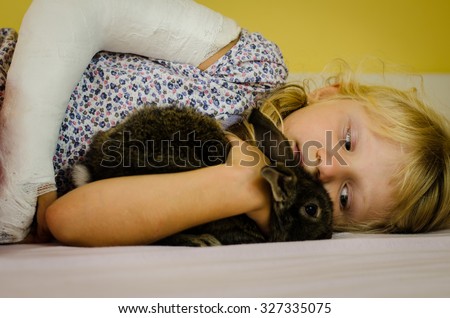hurt blond girl with broken hand lying in bad and holding bunny rabbit pet