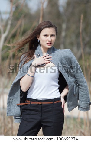 Young woman in the park. Dark haired girl in gray coat posing in park looking at camera