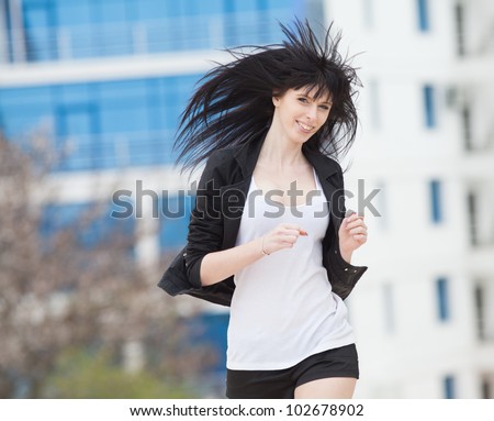 Attractive brunette in black on open air. Young woman in black shorts and jacket runs along the street