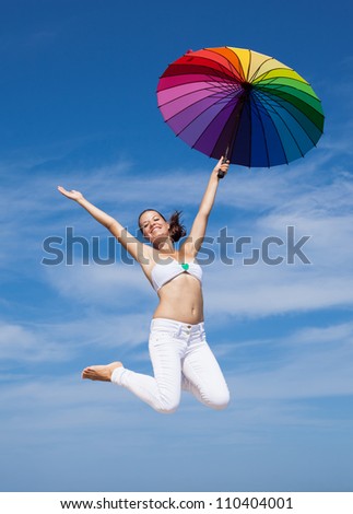 Attractive young woman jumping with parasol. Girl with iridescent umbrella jumping on background of sky