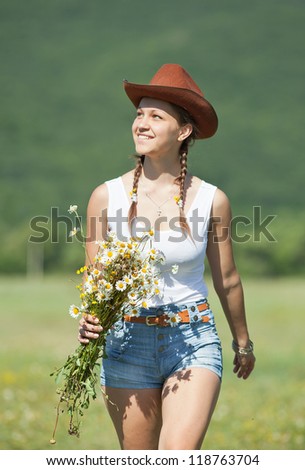 Girl in hat in field. Teenage girl with bouquet of wild chamomile walks along field