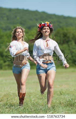 Ukrainian girls in field. Attractive young women in blouses with ukrainian embroidery running along field. Vertical composition