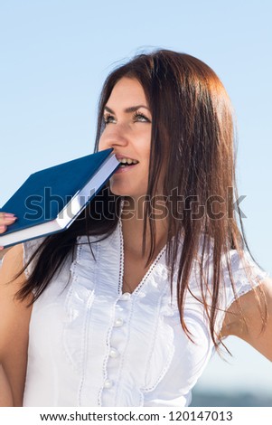 Attractive long haired brunette on open air. Young business woman biting notebook